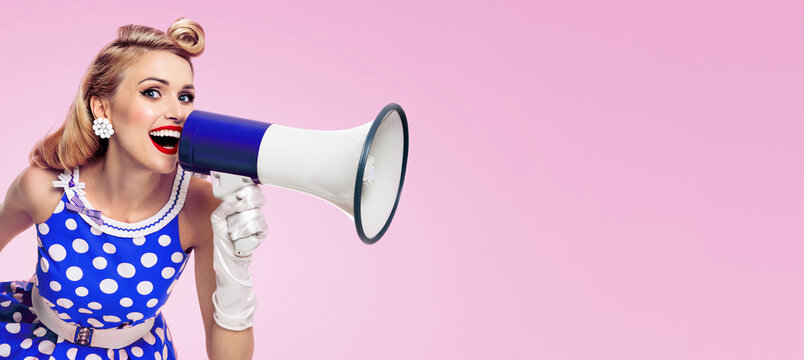 Image of woman holding megaphone, dressed in pin up style blue dress in polka dot white gloves, over pink colour background. Female blond model posing in retro fashion vintage studio concept.
