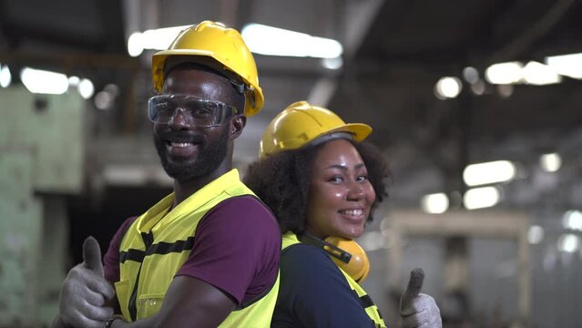 Portrait of group smiling African American industrial worker man and woman with helmet standing back to back show thumbs up in factory .happy confidence black couple employee standing in manufacturing