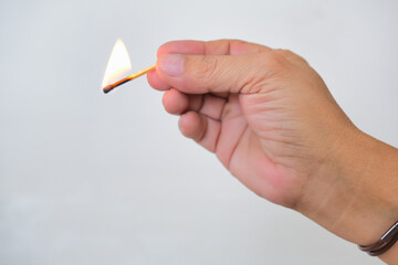 Hand holding a burning matchstick over white background