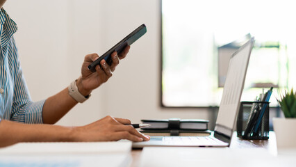 Close up of businesswoman searching business data on smartphone while working on laptop in office