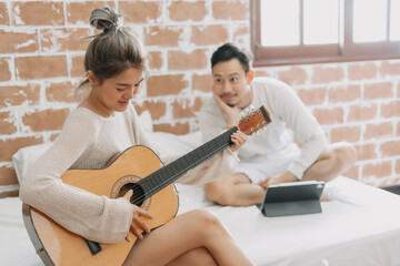 Fototapeta premium Asian man listening to his girlfriend playing guitar on a good hobby weekend.