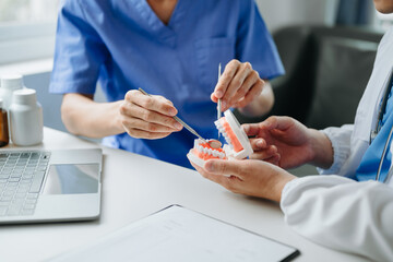 Dentist sitting at table with jaw samples tooth model and working with tablet and laptop in dental office professional dental clinic. medical doctor working.