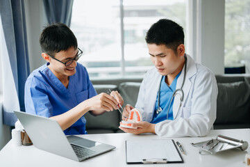 Dentist sitting at table with jaw samples tooth model and working with tablet and laptop in dental office professional dental clinic. medical doctor working.