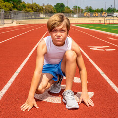 Preteen male track runner with heads up in kneeling stance ready to run a race