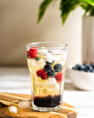 The glass of iced tea with berries on the wooden table. Cuba Libre or long island cocktail, cold drink or lemonade with fruits and basil