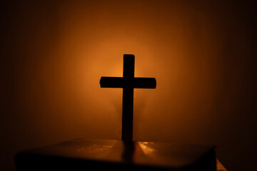 Light candle with holy bible and cross or crucifix on old wooden background in church.Candlelight...