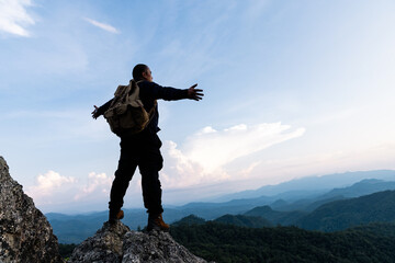 Male tourist on top of rocky mountain. A peaceful man meditating yoga relaxing alone standing and spreading arms on a mountain top at sunrise with nature landscape.