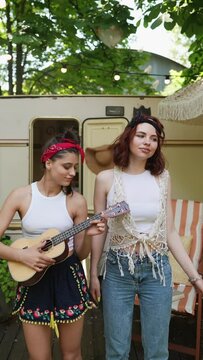 Two free-spirited girls in hippie style playing guitars and singing in harmony.