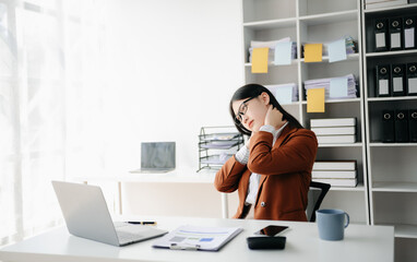 Overworked young Asian businesswoman office worker suffering from neck pain after had a long day at her office desk.