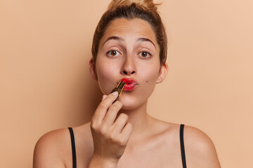 Beauty and cosmetic. Studio shot of young pretty glad European lady applying red lipstick standing...