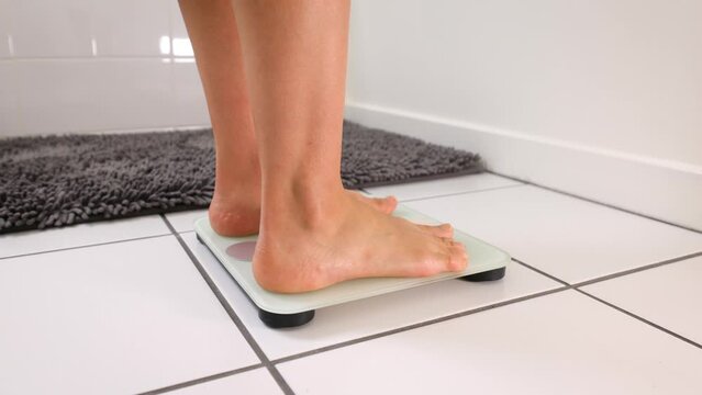 Woman checking her weight by stepping onto a bathroom scale.