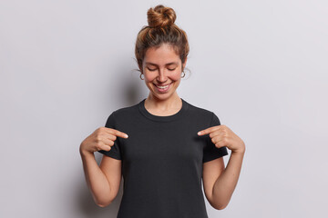 People positive emotions concept. Studio shot of young beautiful happy smiling lady standing isolated in centre on white background wearing black tshirt pointing at chest as space for promotion