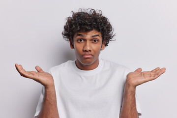 Clueless Hindu man with curly hair has raised palms and shrugged shoulders signify his lack of...