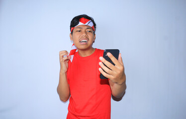 freelance indonesian man angry after got message from his moble phone is squeezing his hand, wearing red t shirt and headband. isolated white