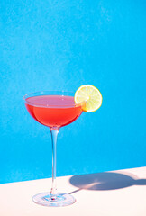 Siesta alcoholic cocktail drink with silver tequila, grapefruit and lime juice, syrup and italian red bitter liqueur, summer blue bright background, hard light and shadows