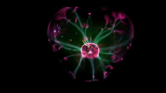 Tesla coil. Plasma globe of heart shape with green and pink light beams. Energy rays moving from side to side. Coil electric discharge. Close-up. Magic object. Plasma Sphere Static Electricity. Decor.