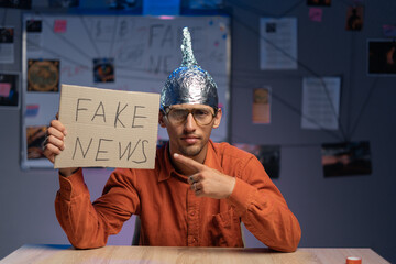 Strange man in a protective foil cap and glasses holding banner with fake news message. Conspiracy...