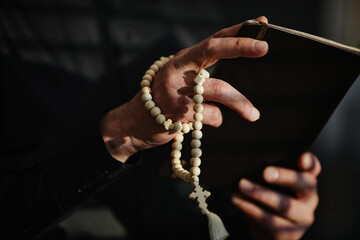 Close up of senior priest holding Bible and rosary while praying in dramatis light, copy space