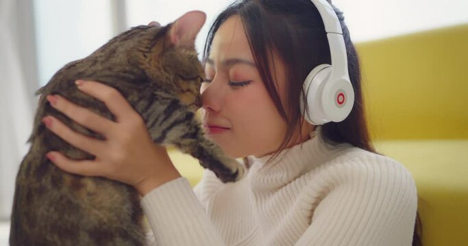 Beautiful woman wearing headset and play with her cat ht home. Beautiful woman holding cat in hand with smile.