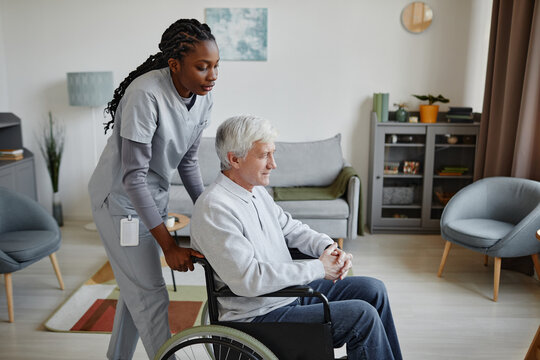 Side view portrait of black young woman assisting senior man with disability in nursing home