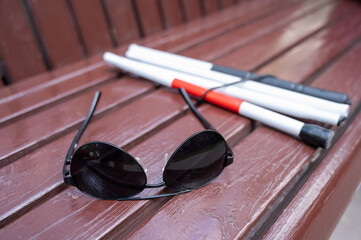 Sunglasses and a folding cane for the blind on a bench. 
