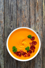 Sweet potatoes cream soup with choriso sausage on wooden background, top view