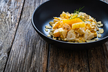 Fruit salad - peaches, pineapples, almonds and corn in mayonnaise on wooden table
