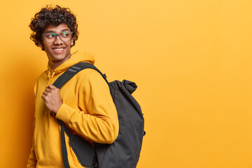 Student lifestyle. Studio sideways shot of young cheerful smiling Hindu male wearing yellow hoodie...