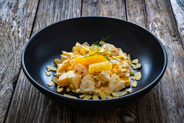 Fruit salad - peaches, pineapples, almonds and corn in mayonnaise on wooden table
