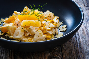 Fruit salad - peaches, pineapples, almonds and corn in mayonnaise on wooden table
