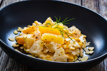 Fruit salad - peaches, pineapples, almonds and corn in mayonnaise on wooden table
