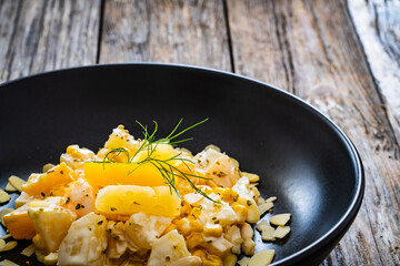 Fruit salad - peaches, pineapples, almonds and corn in mayonnaise on wooden table
