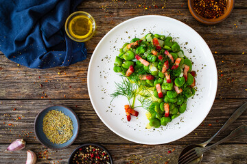 Broad beans with garlic, dill and bacon on wooden table, top view

