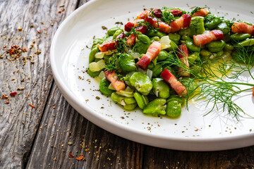 Broad beans with garlic, dill and bacon on wooden table
