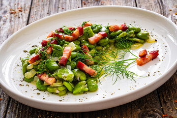 Broad beans with garlic, dill and bacon on wooden table
