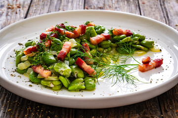 Broad beans with garlic, dill and bacon on wooden table

