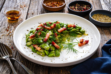 Broad beans with garlic, dill and bacon on wooden table
