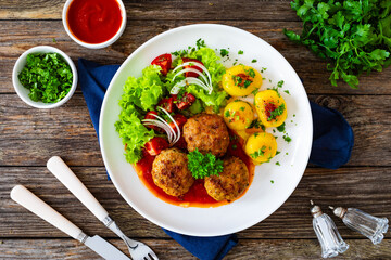 Seared pork meatballs in tomato sauce with fried potatoes  and fresh vegetables on wooden table
