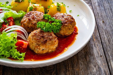 Seared pork meatballs in tomato sauce with fried potatoes  and fresh vegetables on wooden table
