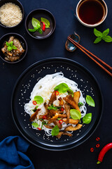 Asian food - fried soy sauce oyster mushrooms with rice noodles on black table, top view