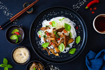 Asian food - fried soy sauce oyster mushrooms with rice noodles on black table, top view