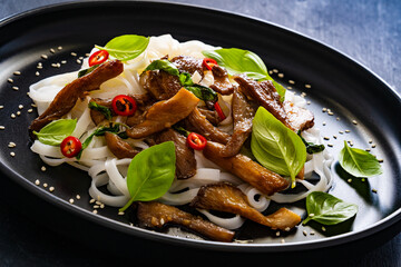 Asian food - fried soy sauce oyster mushrooms with rice noodles on black table
