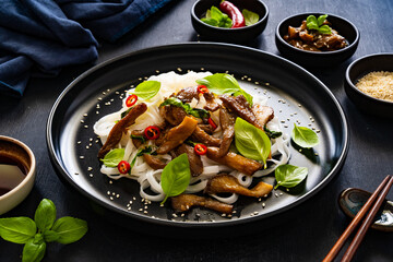 Asian food - fried soy sauce oyster mushrooms with rice noodles on black table
