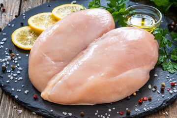 Fresh raw chicken breasts on cutting board with spices on wooden background

