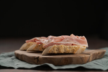 Toassted baguette slices with prosciutto cotto and cream cheese on olive wood board