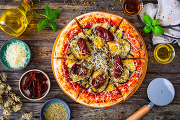 Pizza with eggplant, sun dried tomatoes and parmesan cheese on wooden table
