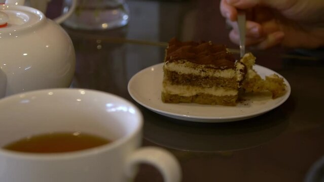 A girl in a cafe breaks off a piece of tiramisu with a fork