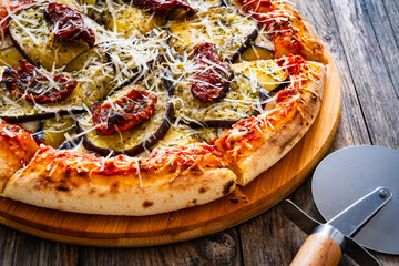 Pizza with eggplant, sun dried tomatoes and parmesan cheese on wooden table
