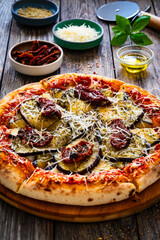 Pizza with eggplant, sun dried tomatoes and parmesan cheese on wooden table
