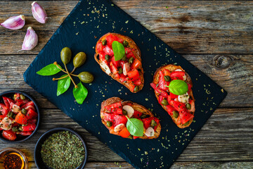 Tasty bruschetta with tomato, capers, garlic and basil leaves on wooden table
